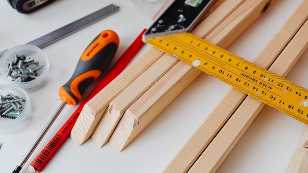 A variety of tools including screws, screwdriver, and ruler on a woodworking table.